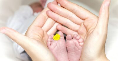 person holding baby's toe with yellow petaled flower in between. it symbolises the love of a caregiver
