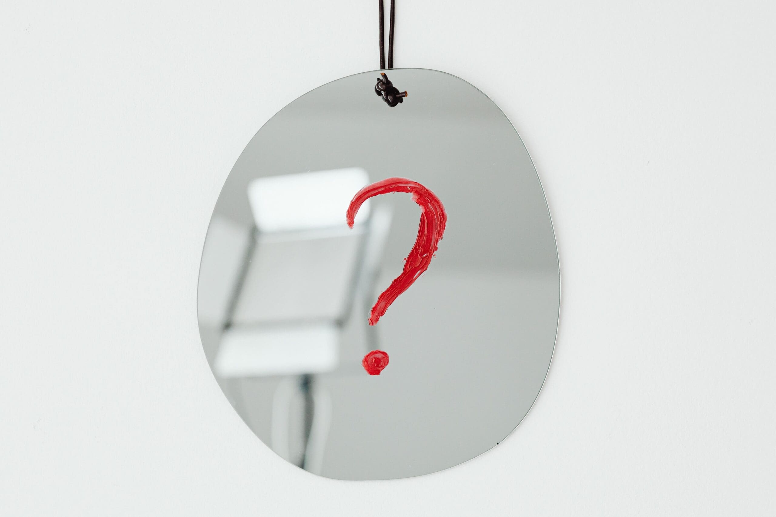 a question mark in red ink written on a round shiny surface hanging by a black thread