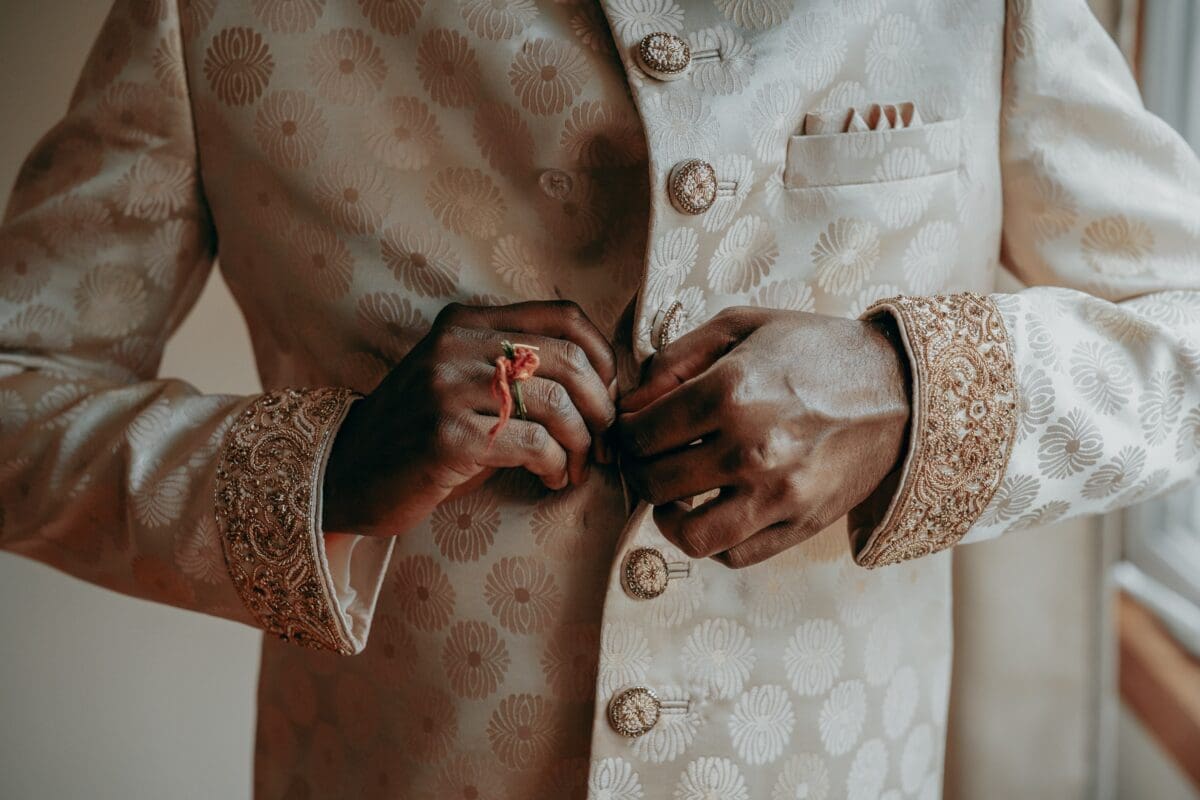 A person buttoning up his traditional Indian bridegroom outfit