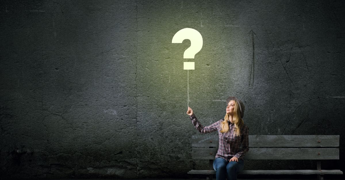 A woman sitting on a bench, holding a balloon the shape of a white question mark