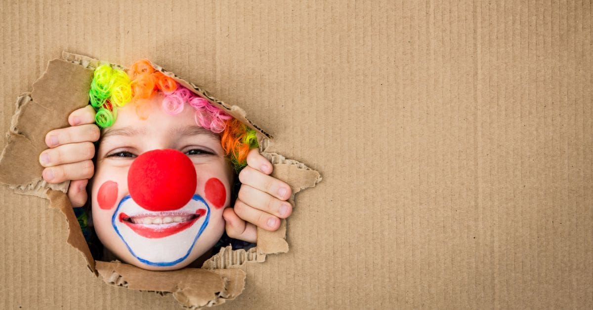 A clown peeking from behind a cardboard sheet