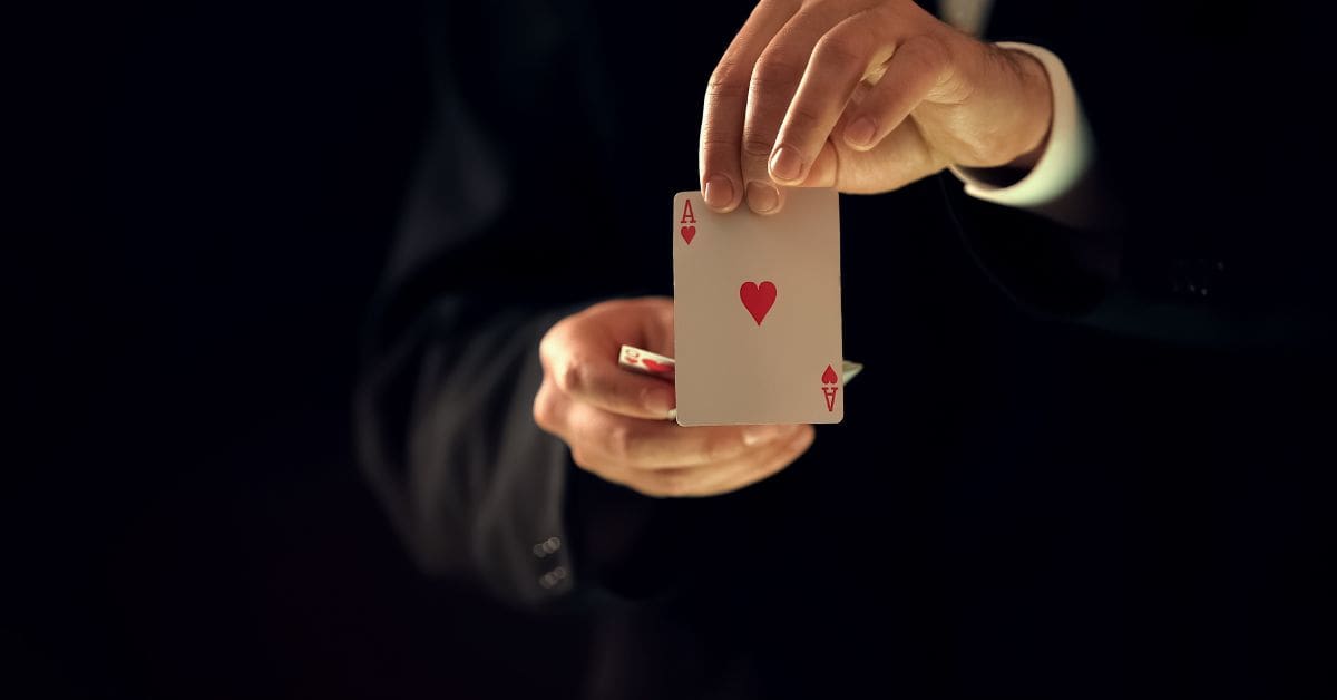 A person's hands visible, holding two playing cards, with ace of heart showing face outside. Likely a magician
